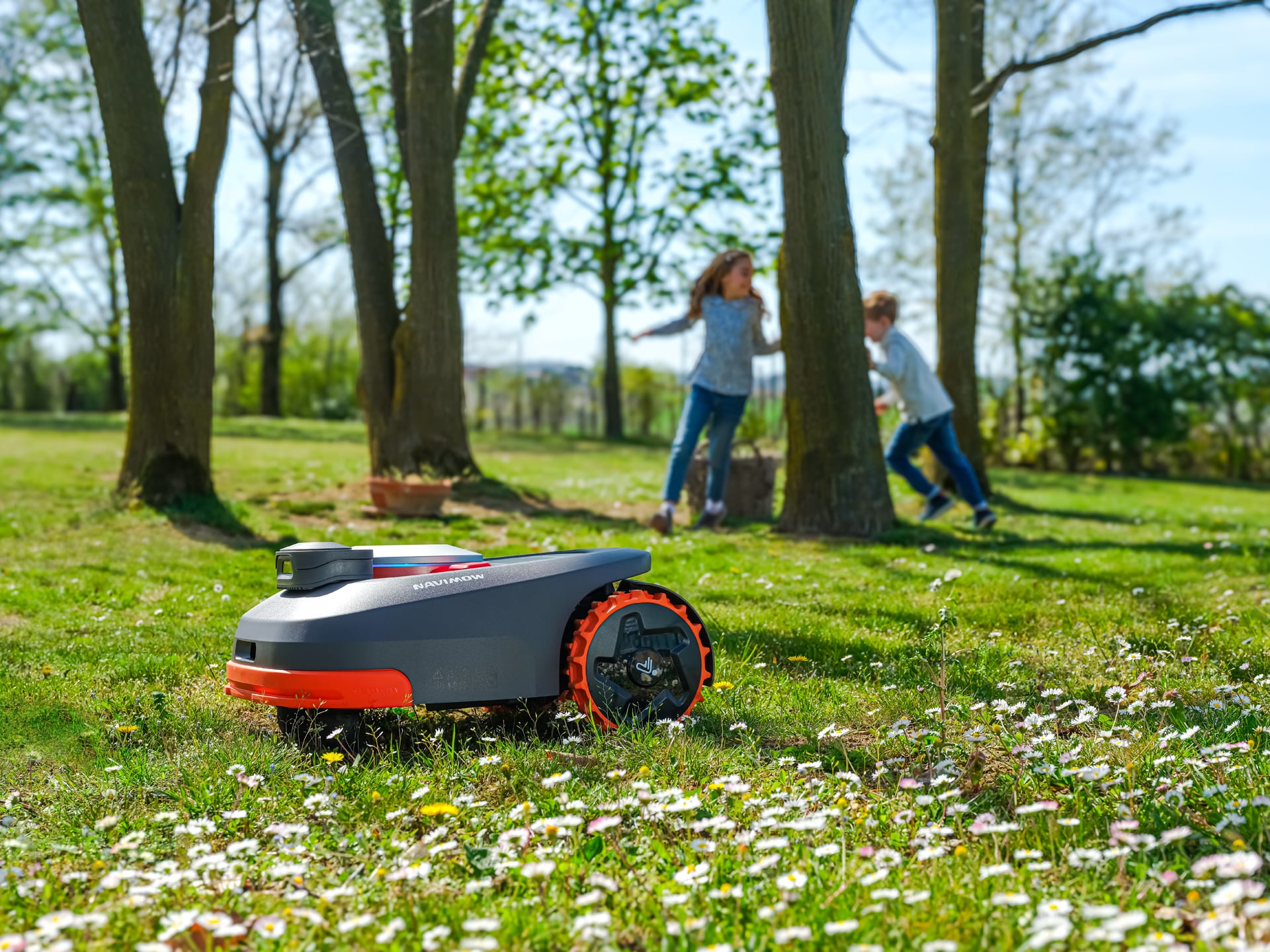 Enfants jouant sur une pelouse tondue uniformément par le Navimow série H visible en arrière-plan - Sécurité et précision technologique compatibles avec les activités familiales.