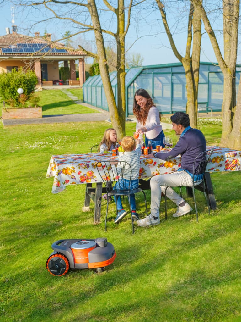Famille savourant un pique-nique pendant que le robot tondeuse Navimow série H entretient leur jardin - Technologie avancée permettant de profiter pleinement des moments en plein air.
