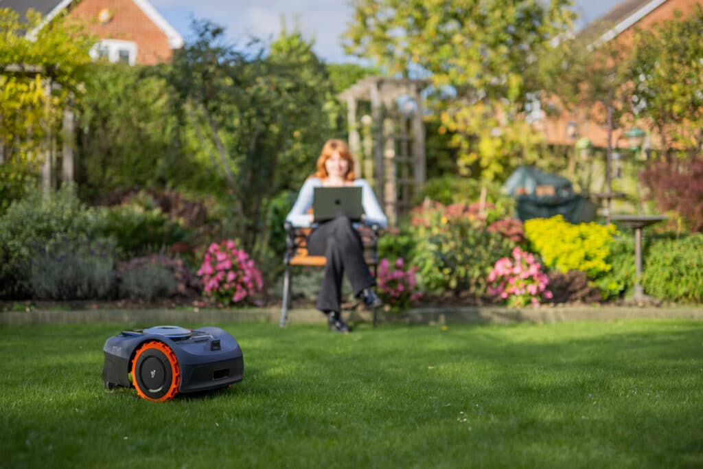 Famille se détendant sur la pelouse pendant que le robot tondeuse Navimow i108 travaille silencieusement - Technologie innovante d'AP Robots permettant de reconquérir du temps libre.